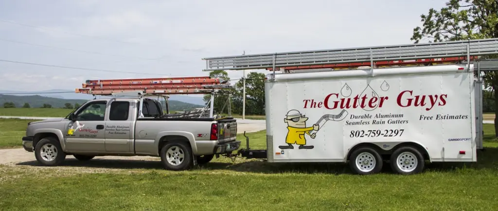 The Gutter Guys pickup truck and enclosed trailer with ladder racks parked in a Vermont field