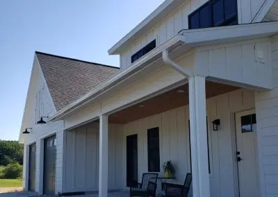 White modern farmhouse in Addison County VT with white seamless gutters along the porch roofline
