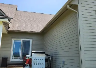 Corner of a sage green Vermont home with a white seamless gutter and downspout