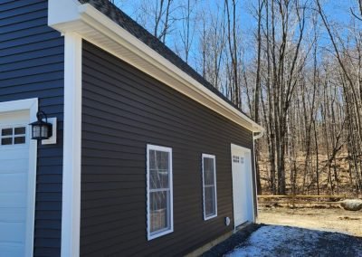 Dark brown garage in Vermont with white seamless gutters along the eave in winter